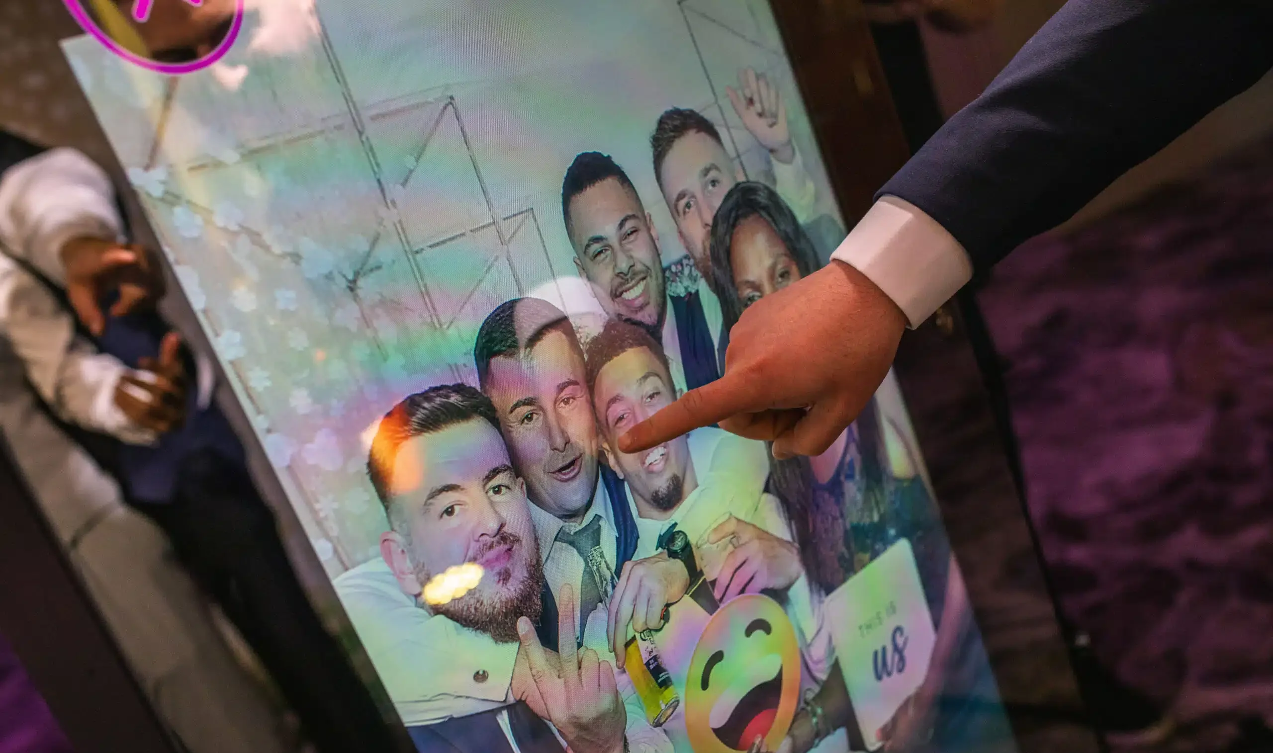 Guest tapping a photo booth screen showing a group photo with emoji stickers