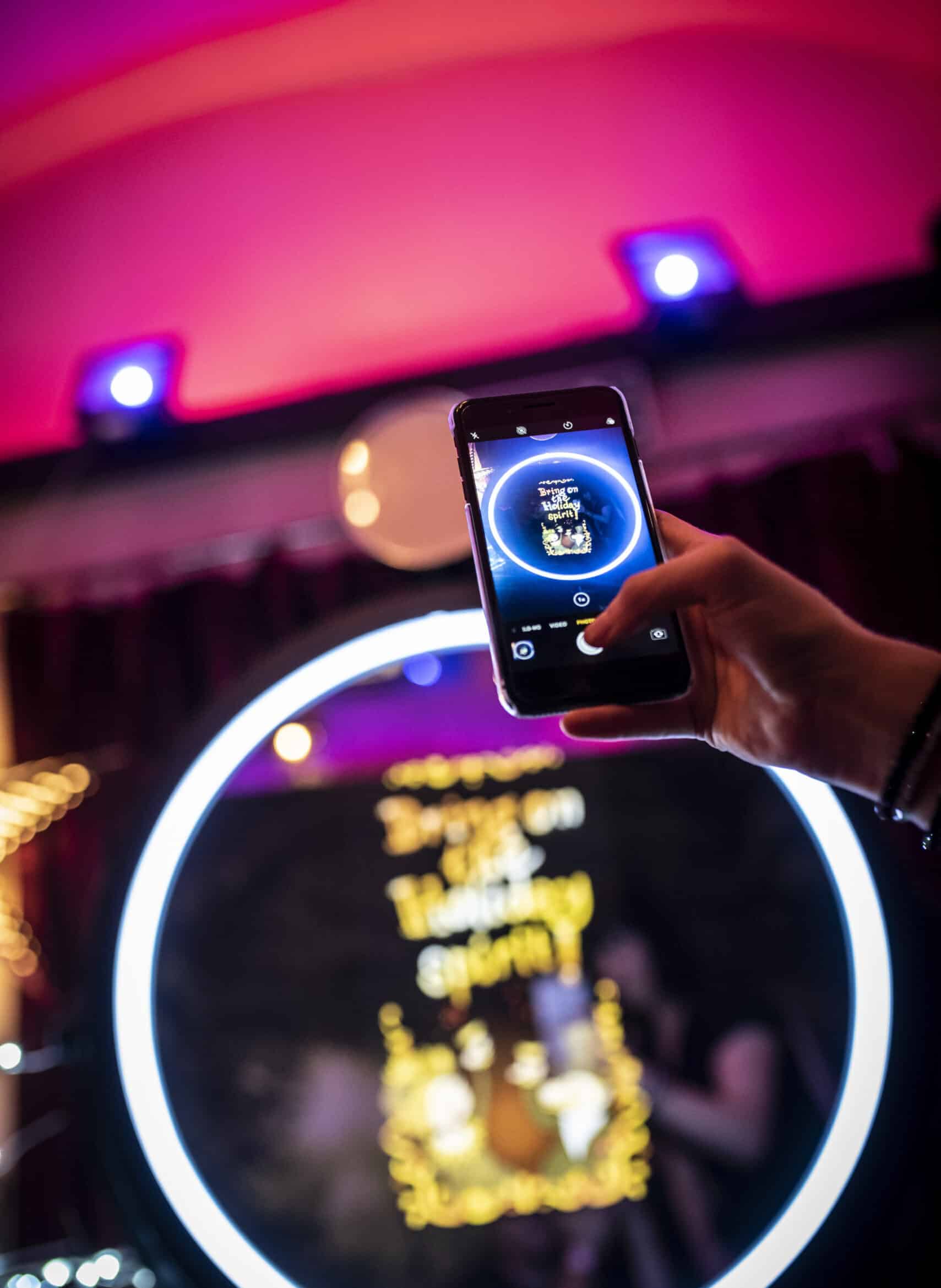 Hand holding a phone displaying a photo booth picture under pink lighting