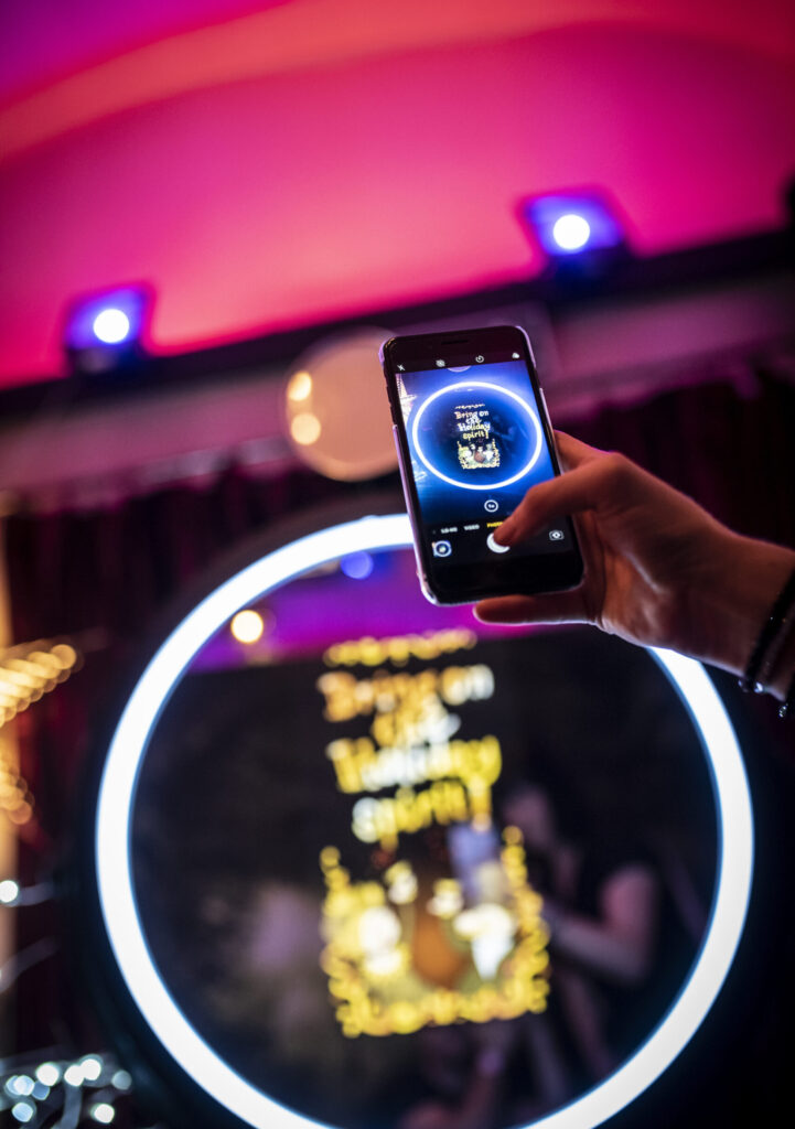 Hand holding a phone above a glowing ring light booth