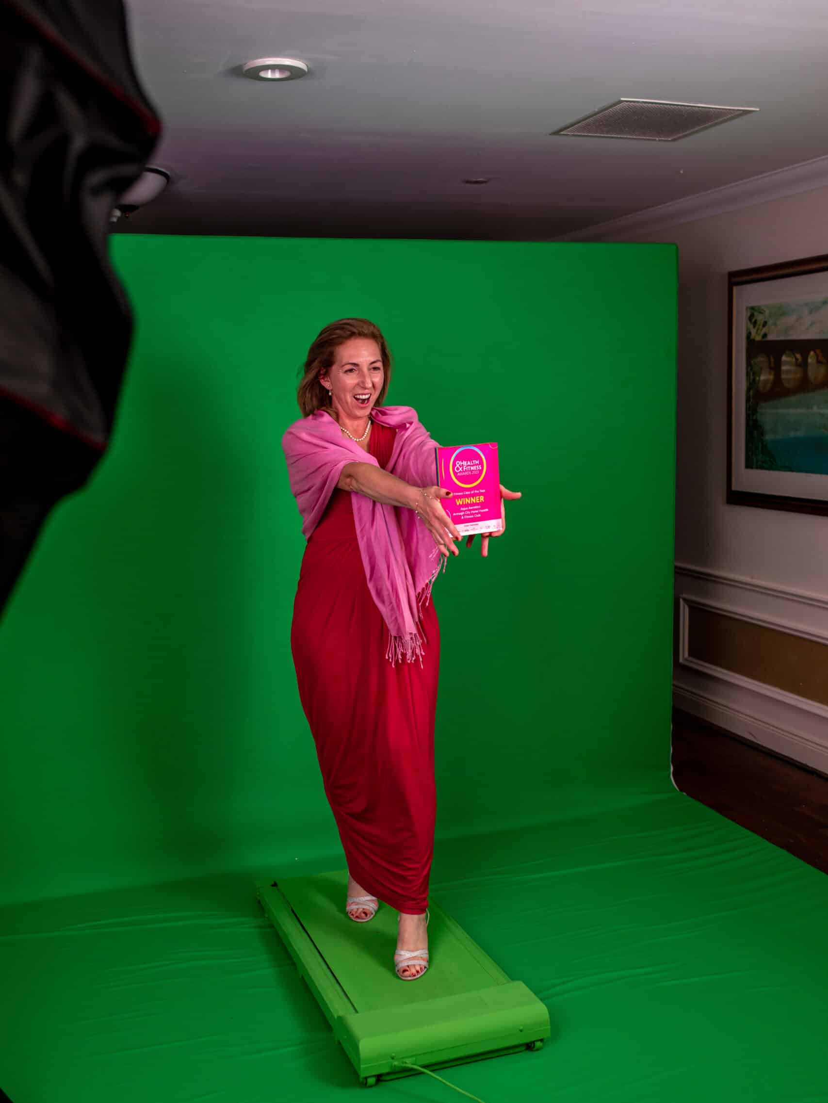 Woman in a red outfit holding a pink prop in front of a green screen