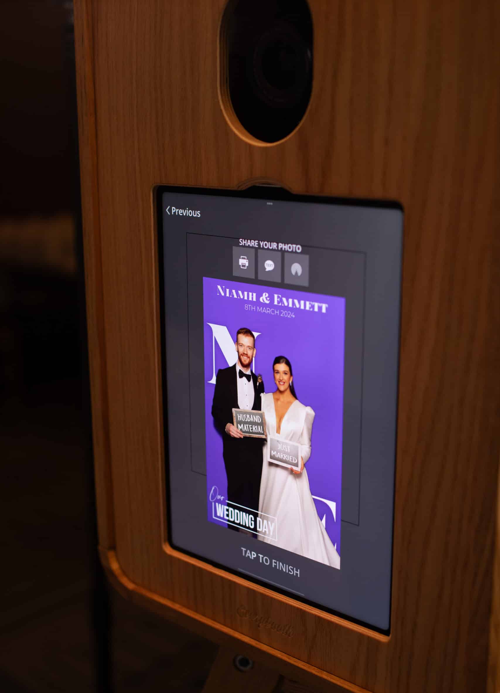 Tablet photo booth in a wooden kiosk displaying a purple welcome screen