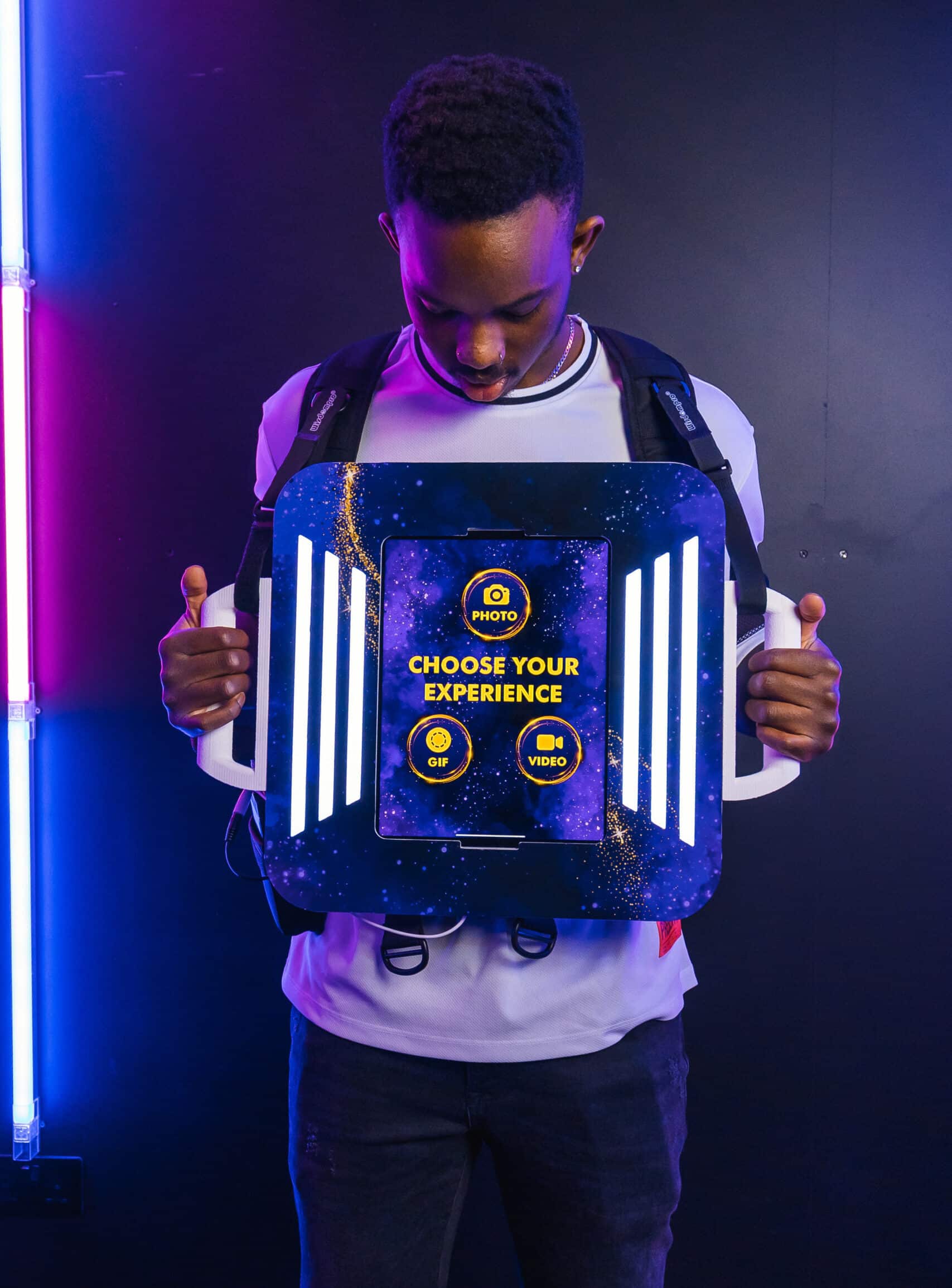 Man standing behind an illuminated photo booth kiosk with a "Choose your experience" screen