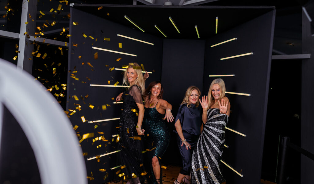 Group of guests dancing at a photo booth with a neon light backdrop