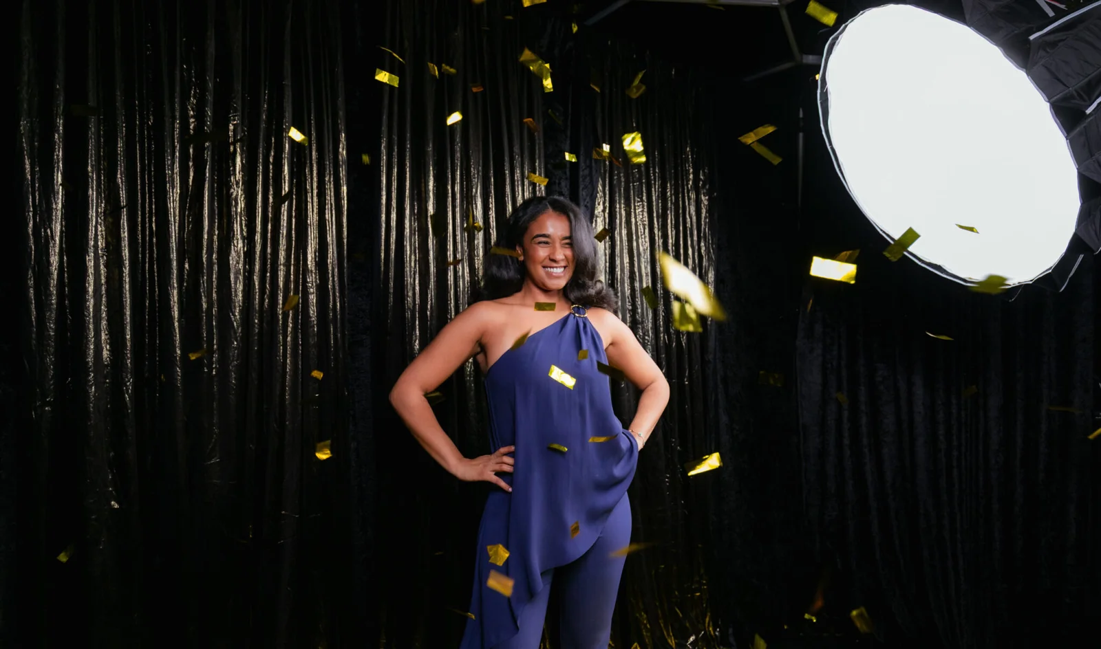 Woman in a blue outfit posing as gold confetti falls against a black backdrop