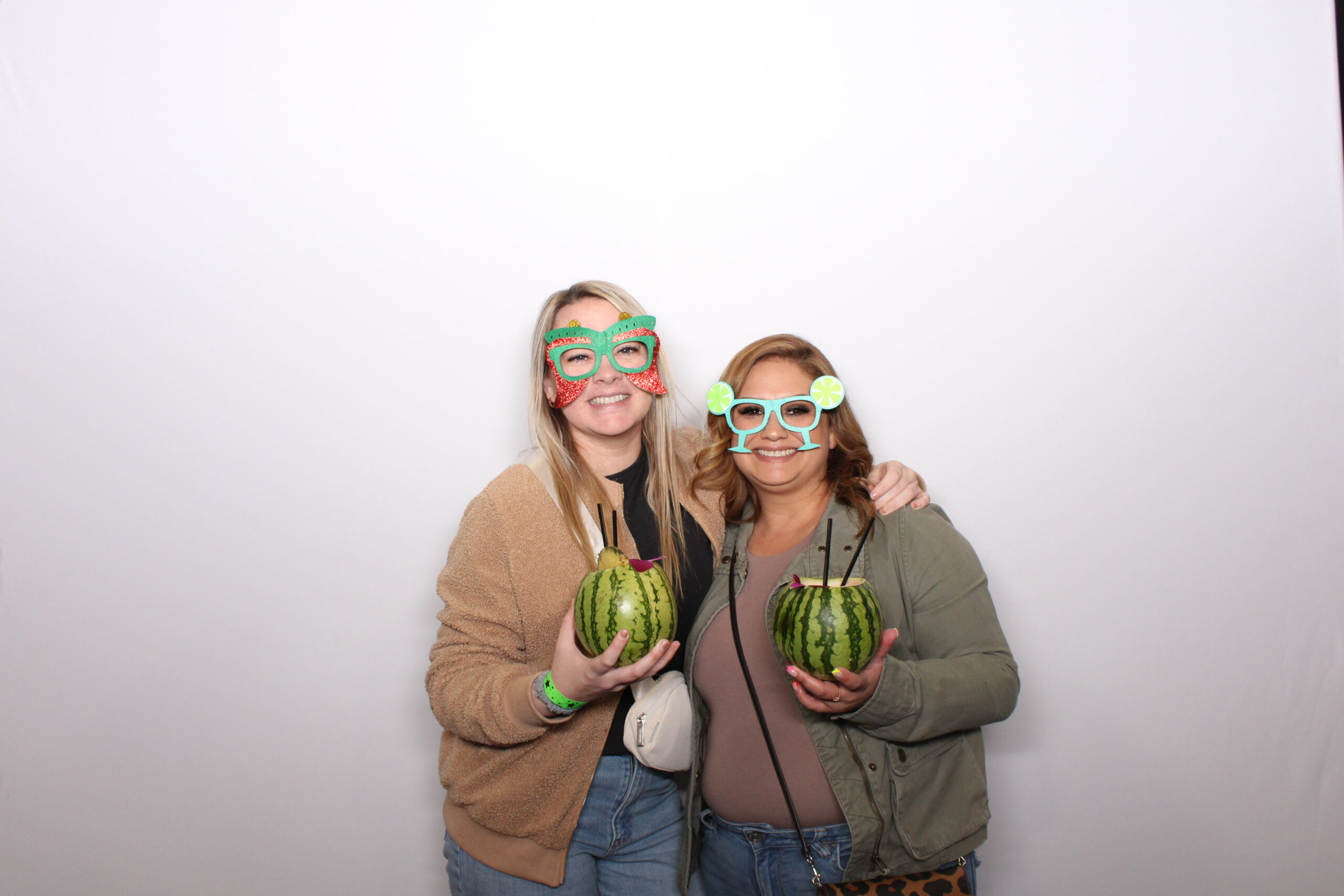 Two women in novelty sunglasses holding watermelon props against a white backdrop