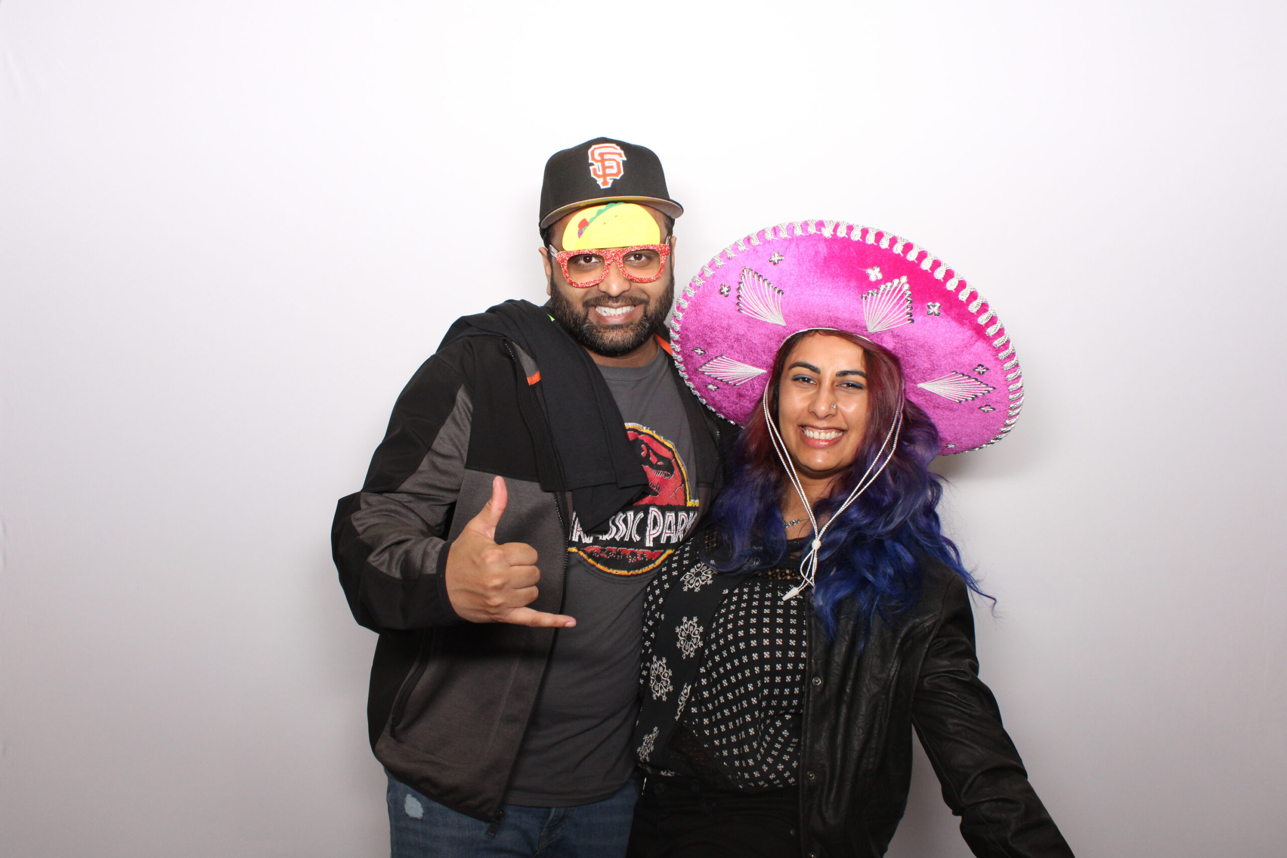 Man in a beanie and woman in a pink sombrero posing with props against a white backdrop