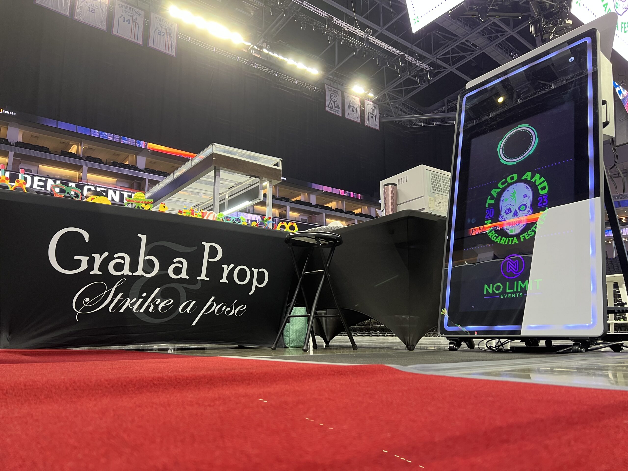 "Grab a Prop, Strike a Pose" sign on a red carpet beside a photo booth in an arena