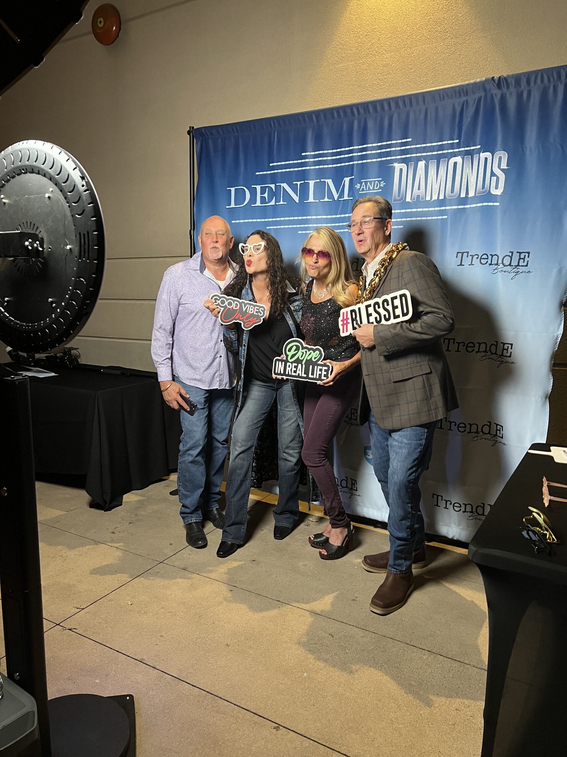 Group posing with props at a photo booth in front of a Denim & Diamonds backdrop