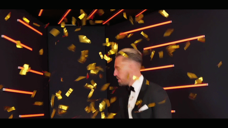 Man in a tuxedo surrounded by falling gold confetti