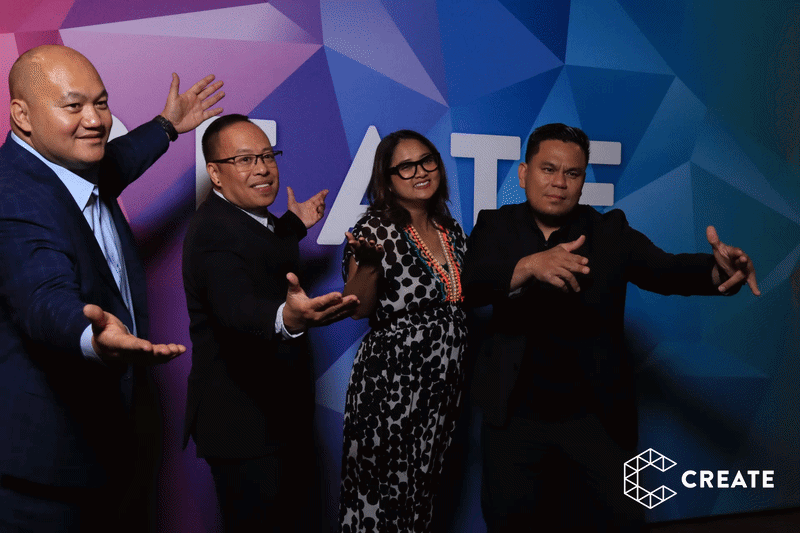 Four guests posing playfully together in front of a colorful geometric step-and-repeat backdrop at a CREATE branded event