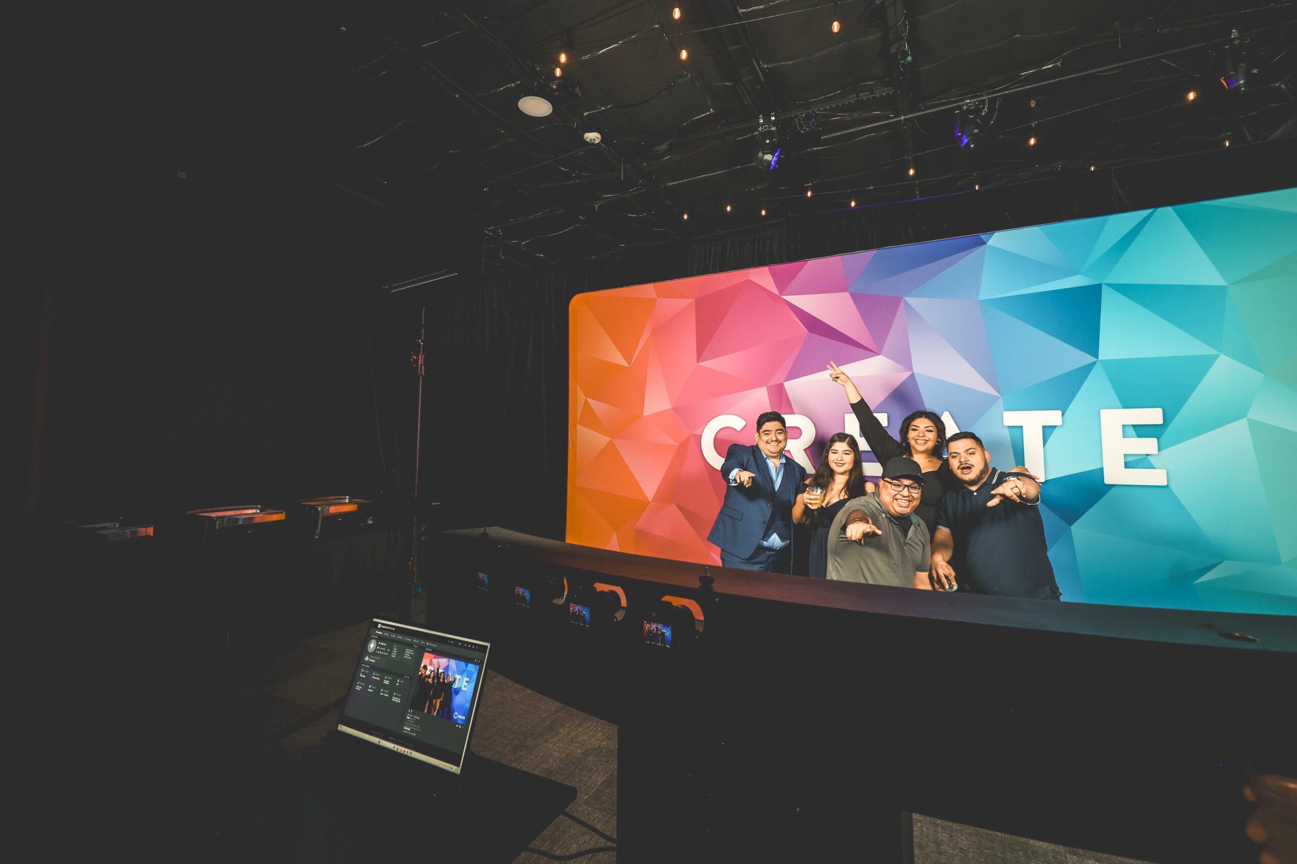 Row of small cameras mounted on a curved arc rig facing a CREATE branded backdrop, with a control laptop in the foreground and five guests posing in the capture zone
