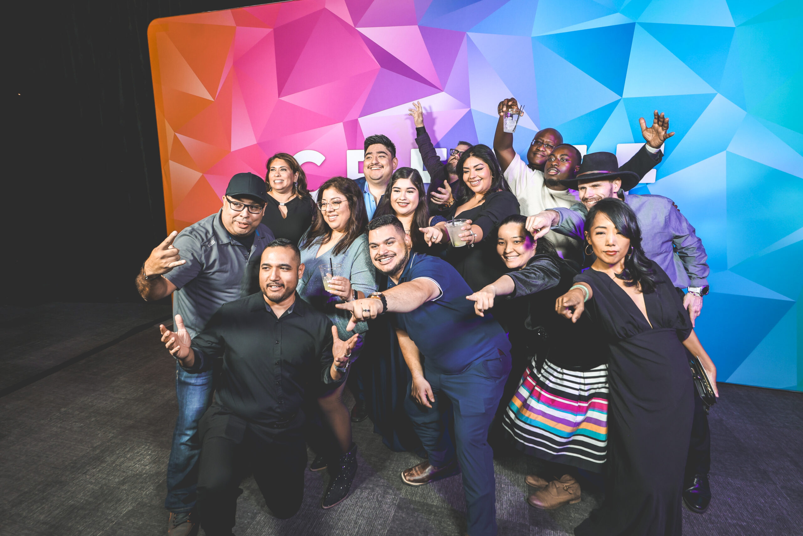 Large group of guests posing and celebrating together in front of a colorful geometric step-and-repeat backdrop at a CREATE branded event